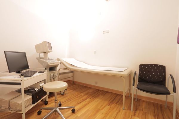 Ein Untersuchungsraum, der mit einem Ultraschallgerät (Sonografie) und einem Computer auf einem Rollwagen ausgestattet ist. In der Mitte des Raumes steht eine Untersuchungsliege für Patienten.